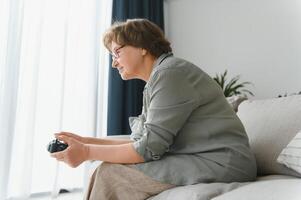 Older person having fun playing a console with a video game sitting on the sofa. photo