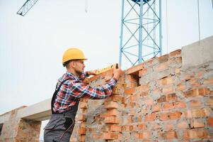 utilizando ladrillos. joven trabajador de la construcción en uniforme está ocupado en el edificio sin terminar foto