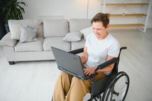 positivo mayor mujer en silla de ruedas trabajando en computadora portátil, eso persona de libre dedicación, en línea foto