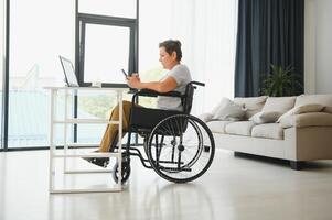 Freelancer in wheelchair using laptop near notebook and papers on table photo