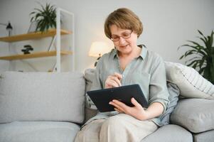 mayor mujer utilizando digital tableta en vivo habitación a hogar foto