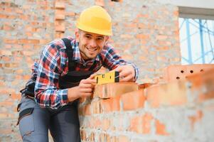 Using bricks. Young construction worker in uniform is busy at the unfinished building photo