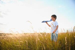 Cute happy cheerful child running fastly along grassy hill at countryside holding big toy plane in hand. Boy playing during sunset time in evening. Horizontal color photography. photo