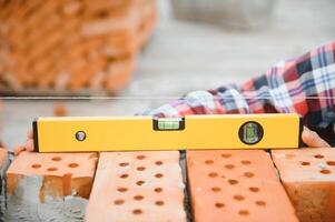 Using bricks. Young construction worker in uniform is busy at the unfinished building photo