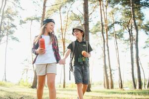 Two happy children having fun during forest hike on beautiful day in pine forest. Cute boy scout with binoculars during hiking in summer forest. Concepts of adventure, scouting and hiking tourism photo