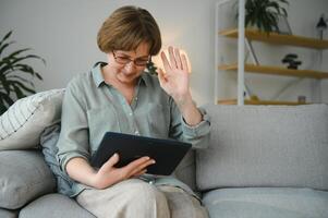 Senior woman looking and laughing at her digital tablet on sofa photo