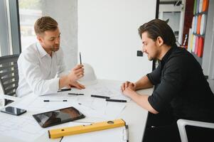 Two colleagues discussing data working on architectural project at construction site at desk in office photo