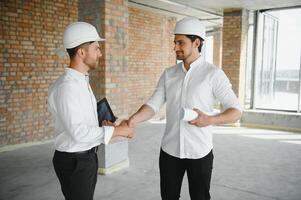 A front view of two smart architects with white helmets reviewing blueprints at a construction site on a bright sunny day photo