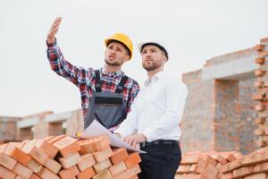 estructural ingeniero y capataz trabajador conversar, plan trabajando para el al aire libre edificio construcción sitio foto