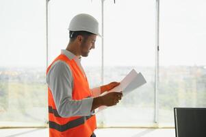 retrato de un arquitecto constructor estudiando diseño plan de el habitaciones, grave civil ingeniero trabajando con documentos en construcción sitio, edificio y hogar renovación, profesional capataz a trabajar. foto