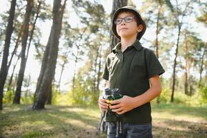 Boy with binoculars. Kid in green forest at summer daytime together. photo