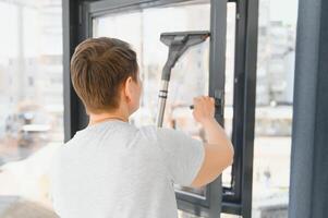 un atractivo de edad mediana mujer es Lavado un ventana en un habitación foto