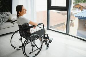 woman looking away while sitting in wheelchair at home photo