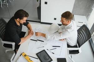 Two colleagues discussing data working on architectural project at construction site at desk in office photo