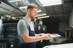 Portrait of production line worker controlling manufacturing process of modern packaging industrial machine in printing factory photo