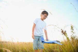 Cute happy cheerful child running fastly along grassy hill at countryside holding big toy plane in hand. Boy playing during sunset time in evening. Horizontal color photography. photo