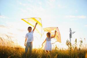 contento niños lanzamiento un cometa en el campo a puesta de sol. pequeño chico y niña en verano vacaciones. foto