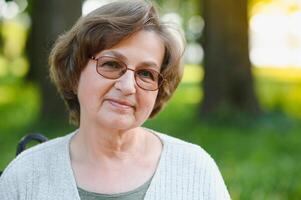 Elegant elderly woman in the shirt is sitting on the bench in a park on a warm day photo