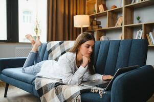 Young woman lying on couch with laptop. photo