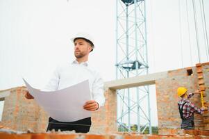 Construction engineer supervising progress of construction project stand on new concrete floor top roof and crane background. photo