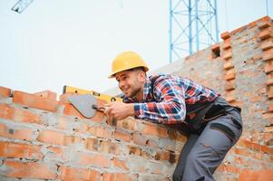 Using bricks. Young construction worker in uniform is busy at the unfinished building photo