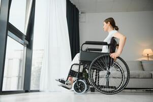 joven mujer en silla de ruedas a hogar en vivo habitación. foto