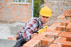 utilizando ladrillos. joven trabajador de la construcción en uniforme está ocupado en el edificio sin terminar foto