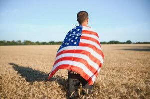 joven hombre participación americano bandera, en pie en trigo campo foto