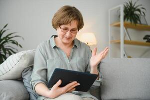 Senior woman on the sofa in her apartment or retirement home with tablet computer online photo