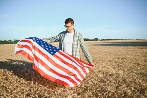 joven hombre participación americano bandera, en pie en trigo campo foto