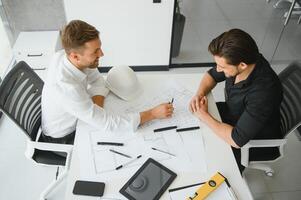 Two colleagues discussing data working on architectural project at construction site at desk in office photo