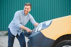 sonriente hombre desenchufar el cargador desde el coche foto