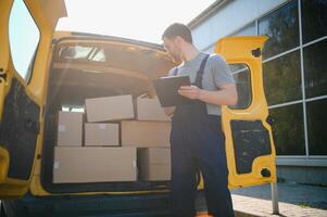 joven entrega hombre mensajero en uniforme sostener documentos portapapeles comprobación lista paquete o empaquetar enviar cajas cerca un coche para Servicio envío a cliente, en línea compras Servicio conceptos. foto