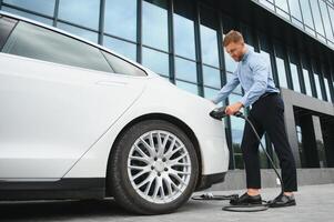 portrait of young handsome bearded man in casual wear, standing at the charging station and holding a plug of the charger for an electric car. Eco electric car concept. photo