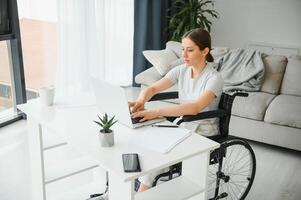 Freelancer in wheelchair using laptop near notebook and papers on table photo