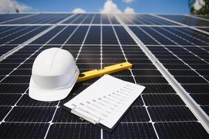 Solar cell contractor document with orange engineering team helmet on solar cells panels. Renewable energy and ecology concept. photo