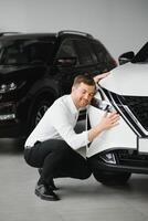 Visiting car dealership. Handsome bearded man is stroking his new car and smiling. photo