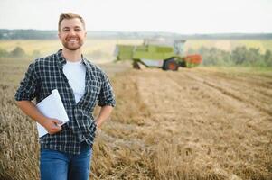 Handsome farmer with tablet standing in front of combine harvester during harvest in field. photo