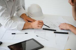 Two young architects with blueprints of a house standing in office, talking. photo