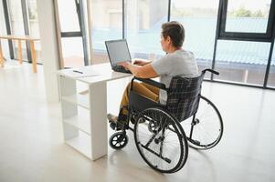 Middle age woman using laptop sitting on wheelchair at home photo