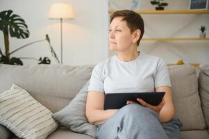 gente, tecnología y Internet concepto - contento medio Envejecido mujer con tableta ordenador personal computadora a hogar. foto