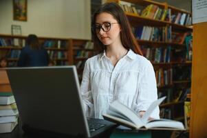 Universidad biblioteca hermosa inteligente caucásico niña usos computadora portátil, escribe notas para papel, ensayo, estudiar para clase asignación. enfocado estudiantes aprendiendo, estudiando para Universidad exámenes lado ver retrato foto