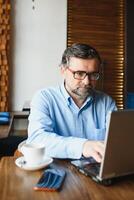 Business, technology and people concept , senior businessman with laptop computer drinking coffee at modern cafe. photo