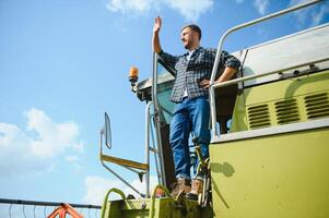 Harvester machine driver climbing into a cab to harvest his wheat field. Farmer getting in combine on ladder holding railing. Agronomist. Rancher after harvesting work photo