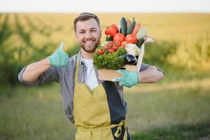 farmer holding a crate of bio vegetables in the farm. Happy man showing box of harvested vegetables. photo