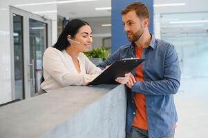 The employee of the beauty salon meets the client in the reception of a modern beauty salon. A man signs a paper with the consent for maintenance. The woman smiles at him photo