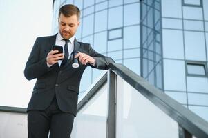 Bearded businessman in formal suit on break using mobile phone use smartphone. business man standing outside on modern urban city street background with coffee cup in downtown outdoors. copy space photo