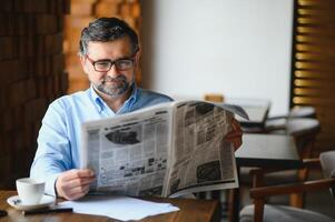 active senior man reading newspaper and drinking coffee in restaurant photo