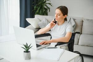 Female freelance programmer sitting in wheelchair and using computers while coding web game at home. photo