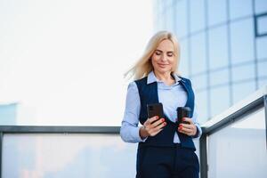 Beautiful Woman Going To Work With Coffee Walking Near Office Building. Portrait Of Successful Business Woman Holding Cup Of Hot Drink. photo